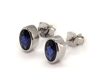 May include: A pair of silver stud earrings with a dark blue gemstone in each. The earrings are marked with "925" on the back.