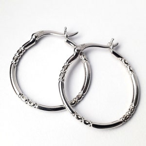 May include: A pair of silver hoop earrings with a textured design. The earrings are made of metal and have a polished finish.