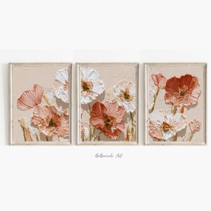 May include: Set of three framed floral art prints. Each print features textured, impasto-style flowers in shades of peach, white, and rust against a neutral background. The artwork is displayed in light-colored wooden frames, creating a cohesive wall art set.