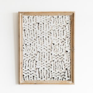 Peut inclure: Une &oelig;uvre d'art abstraite blanche encadr&eacute;e avec un motif textur&eacute; et tiss&eacute;. Le cadre est en bois clair.