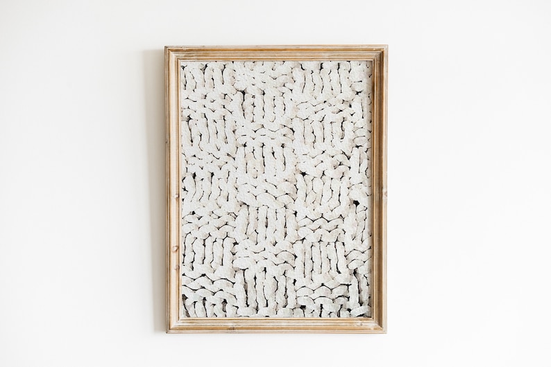 Peut inclure: Une &oelig;uvre d'art abstraite blanche encadr&eacute;e avec un motif textur&eacute; et tiss&eacute;. Le cadre est en bois clair.