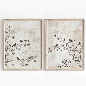 May include: A set of two framed prints with a beige background and a silhouette of a tree branch with birds. The frames are white with a distressed finish.
