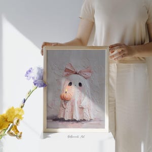 May include: A framed painting of a ghost with a pink bow, holding a pumpkin with a lit candle. The ghost is white with pink accents. The artwork is signed "BeBroccole Art".