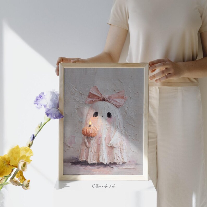 May include: A framed painting of a ghost with a pink bow, holding a pumpkin with a lit candle. The ghost is white with pink accents. The artwork is signed "BeBroccole Art".