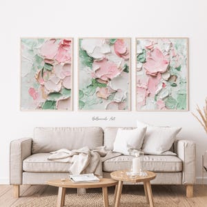 Könnte beinhalten: Drei gerahmte Kunstdrucke mit floralen Motiven und strukturierten Pinselstrichen in Rosa-, Weiß- und Grüntönen. Das Kunstwerk wird über einem beigen Sofa mit Holztischen ausgestellt. Die Signatur des Künstlers, "BelBriccole Art", ist sichtbar.