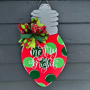May include: A red and green lightbulb-shaped Christmas door hanger with white polka dots and the text "merry and bright".