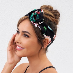 Könnte beinhalten: Eine Frau mit braunen Haaren trägt ein schwarzes und grünes Blumenhaarband. Das Haarband ist oben auf ihrem Kopf zu einem Knoten gebunden. Das Haarband hat einen weißen Hintergrund mit grünen Blättern und rosa Blüten.