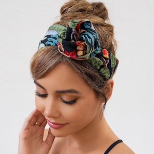 Könnte beinhalten: Ein schwarzes Blumenstirnband mit einer großen Schleife. Das Stirnband hat ein farbenfrohes Muster aus roten, grünen und blauen botanischen Elementen. Der Text "@JuneStudioDesign" ist unten rechts sichtbar.
