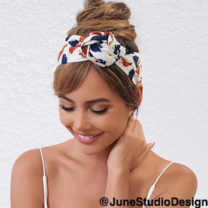 May include: A woman with brown hair is wearing a white headband with a blue and orange floral pattern. The headband is tied in a knot on top of her head. She is smiling and looking down.