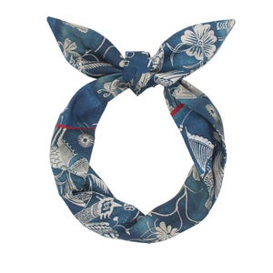 Op de afbeelding: Een blauw-witte hoofdband met patroon, met een geknoopte bovenkant en strikvormige uiteinden. De stof heeft een herhalend bloemen- en vogelontwerp met rode accentstrepen. De hoofdband is ontworpen om om het hoofd te worden gedragen.