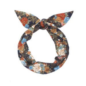 Könnte beinhalten: Ein Stirnband mit Blumenmuster und Schleife. Das Stirnband hat einen dunkelmarineblauen Hintergrund mit einem farbenfrohen Blumendesign in Rot, Orange, Blau und Weiß. Die Schleife ist oben gebunden.