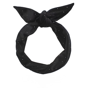 Könnte beinhalten: Ein schwarzes Stirnband mit weißen Tupfen. Das Stirnband ist oben mit zwei spitzen Enden verknotet. Der Stoff scheint weich zu sein. Ein schlichtes und klassisches Design.