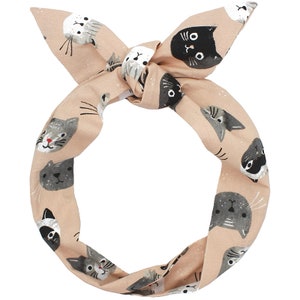 Könnte beinhalten: Ein hellrosa Stirnband mit einem Muster aus verschiedenen Katzen in Schwarz, Weiß und Grau. Das Stirnband ist oben zu einem Knoten gebunden.