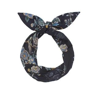 Könnte beinhalten: Ein dunkelmarineblaues Stirnband mit einem Blumenmuster mit blauen, gelben und grünen Blumen und Blättern. Das Stirnband ist oben mit einer Schleife gebunden. Der Stoff hat einen seidigen Glanz.
