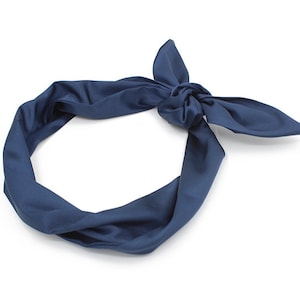 Puede incluir: Una diadema de tela azul oscuro atada en un lazo. La diadema está hecha de un material suave y liso.