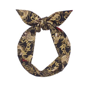 May include: Black and gold patterned headband with a knotted bow. The fabric features a repeating design of koi fish, maple leaves, and swirling patterns. The headband is a stylish accessory.
