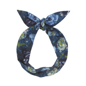 May include: A blue floral headband with a knotted top. The fabric features a dark blue background with a pattern of blue, green, and white flowers. The headband is designed to be worn around the head.