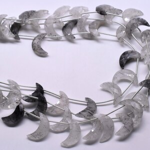 May include: A strand of crescent moon shaped beads made of clear quartz with black inclusions. The beads are strung on silver wire.