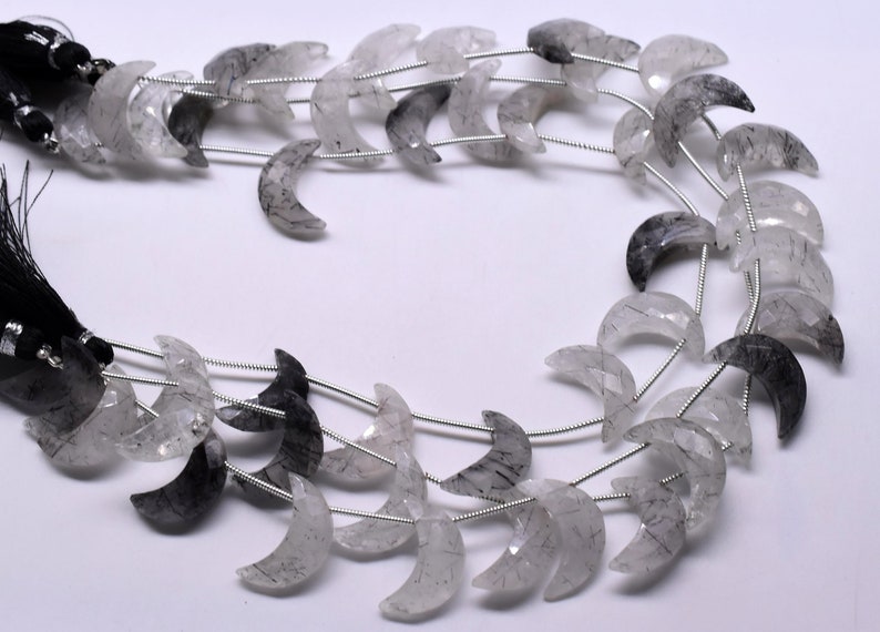 May include: A strand of crescent moon shaped beads made of clear quartz with black inclusions. The beads are strung on silver wire.
