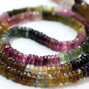 May include: A strand of multi-colored gemstone beads, including pink, green, brown, and black. The beads are faceted and have a slightly irregular shape.