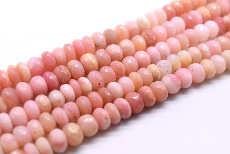 May include: A strand of pink opal beads, faceted and polished, with a slightly irregular shape. The beads are strung together on a clear thread.