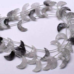 May include: A strand of crescent moon shaped beads made of clear quartz with black inclusions. The beads are strung on silver wire.