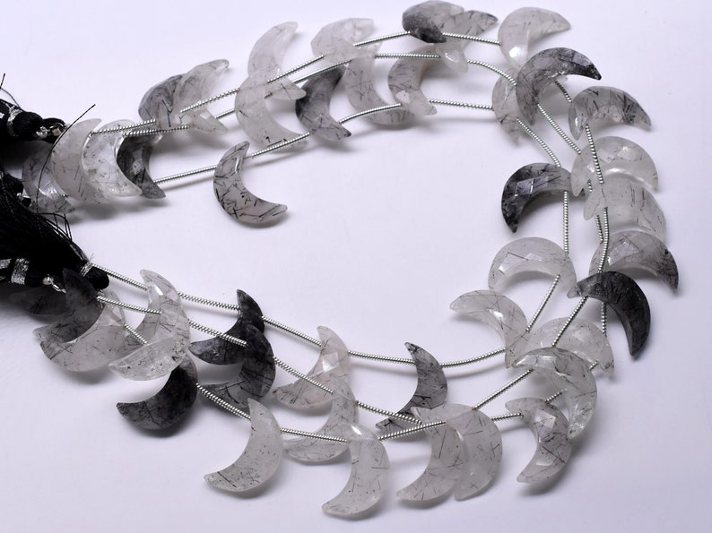 May include: A strand of crescent moon shaped beads made of clear quartz with black inclusions. The beads are strung on silver wire.