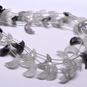 May include: A strand of crescent moon shaped beads made of clear quartz with black inclusions. The beads are strung on silver wire.
