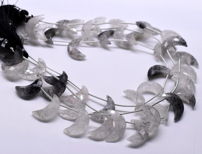 May include: A strand of crescent moon shaped beads made of clear quartz with black inclusions. The beads are strung on silver wire.
