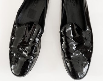 Könnte beinhalten: Paar glänzende schwarze Leder-Loafer. Die Schuhe haben eine runde Spitze und einen niedrigen Absatz. Der Markenname Gucci ist auf der Innensohle aufgedruckt. Die Schuhe sind vor einem weißen Hintergrund platziert.