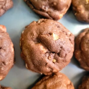 Puede incluir: Primer plano de varias galletas con chispas de chocolate. Las galletas son de color marrón oscuro con chispas de chocolate visibles. Las galletas están dispuestas sobre una superficie azul claro.