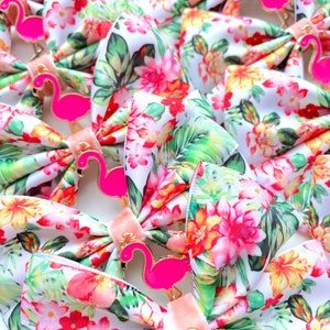 May include: A collection of white fabric bows with a tropical floral print and pink flamingo accents. The bows are tied with a pink ribbon.