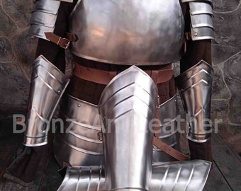 May include: A set of silver-colored medieval armor, including a chest plate, shoulder plates, and leg guards. The armor is made of metal and has a polished finish. The armor is displayed on a wooden surface.