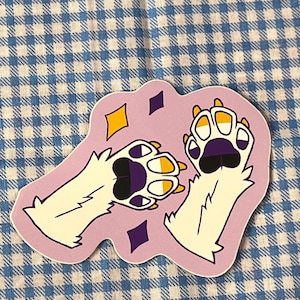 May include: A sticker featuring two cartoon paw prints with white fur, purple paw pads, and yellow and white claws. The sticker has a light purple background with yellow and purple diamond shapes.