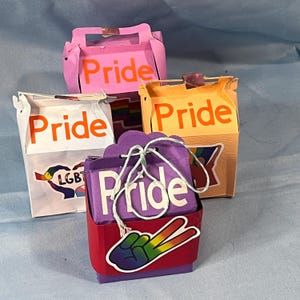 May include: A collection of colorful Pride-themed gift boxes. The boxes are in various colors, including pink, orange, and purple, with the word "Pride" in orange. Some boxes have LGBT-themed stickers and a peace sign.