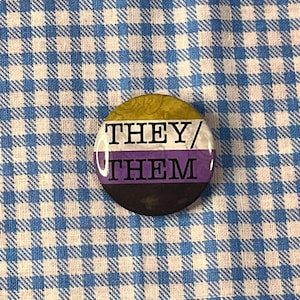 May include: A white ceramic mug with a black handle and the text "But First, Coffee" in a bold, black font. The mug is set against a blurred background, suggesting a cozy setting.