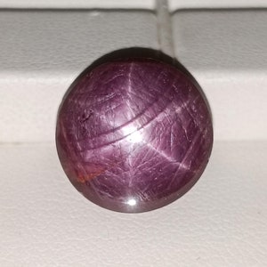 Puede incluir: Una piedra preciosa de rubí estrella rojo oscuro con una estrella de seis puntas en el centro. El rubí es redondo y de corte cabujón.