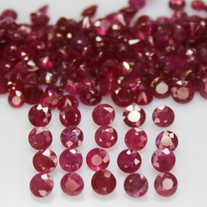 May include: A collection of faceted, deep red gemstones, likely rubies, scattered across a white surface. The gems vary in size and shape, with a few arranged in neat rows. The overall effect is one of luxury and natural beauty.