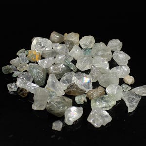 以下が含まれることがあります： クリアでライトグリーンの粗いアクアマリンの宝石のコレクション。石はさまざまなサイズと形があり、一部はわずかに虹色の輝きを放っています。