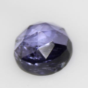 Peut inclure: Une pierre précieuse taillée en forme de goutte d'eau, de couleur violette profonde. La surface de la gemme reflète la lumière, révélant ses multiples facettes et sa structure interne. La pierre est polie.
