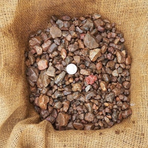 May include: A burlap sack filled with a variety of small, brown, red, and gray stones. A white coin is visible in the center of the pile of stones.