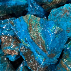May include: A close-up of a large piece of blue and green chrysocolla. The stone has a smooth, polished surface and a variety of textures. The blue color is vibrant and the green is a more muted shade.