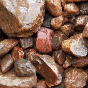 May include: Close-up of a pile of wet, smooth river rocks. The rocks vary in size and shape, with colors ranging from reddish-brown to tan. The surface of the rocks glistens, suggesting they are recently wet.
