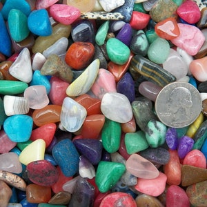 May include: A collection of colorful tumbled stones, including green, blue, red, pink, and yellow. The stones are various shapes and sizes, and some have a shiny, polished finish. A US quarter is included for scale.