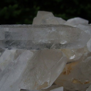 May include: A pile of clear quartz crystals, some with a slight milky hue. The crystals are various sizes and shapes, with some having a pointed tip.