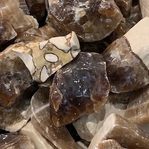 May include: A close-up of a pile of brown and white calcite crystals. The crystals are rough and have a natural, unpolished look.