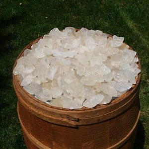 May include: A wooden barrel filled with clear quartz crystals. The crystals are various sizes and shapes, and they are all very shiny.