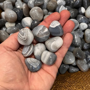 May include: A collection of gray and white agate tumbled stones. The stones are smooth and polished, with a variety of patterns and textures.