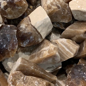 May include: A close-up of a pile of brown and white banded calcite crystals. The crystals are rough and have a natural, unpolished look.