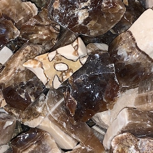 May include: A close-up of a pile of brown and white gemstone chips. The chips are irregular in shape and have a variety of textures. Some of the chips have a more polished finish, while others are more rough.
